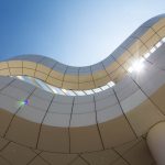 Looking up at the curved side of a white building with sun peaking through a gap