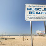 sign of muscle beach with sand and ocean in the background