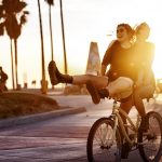one woman riding a back while another woman sits on the handle bars during sunset