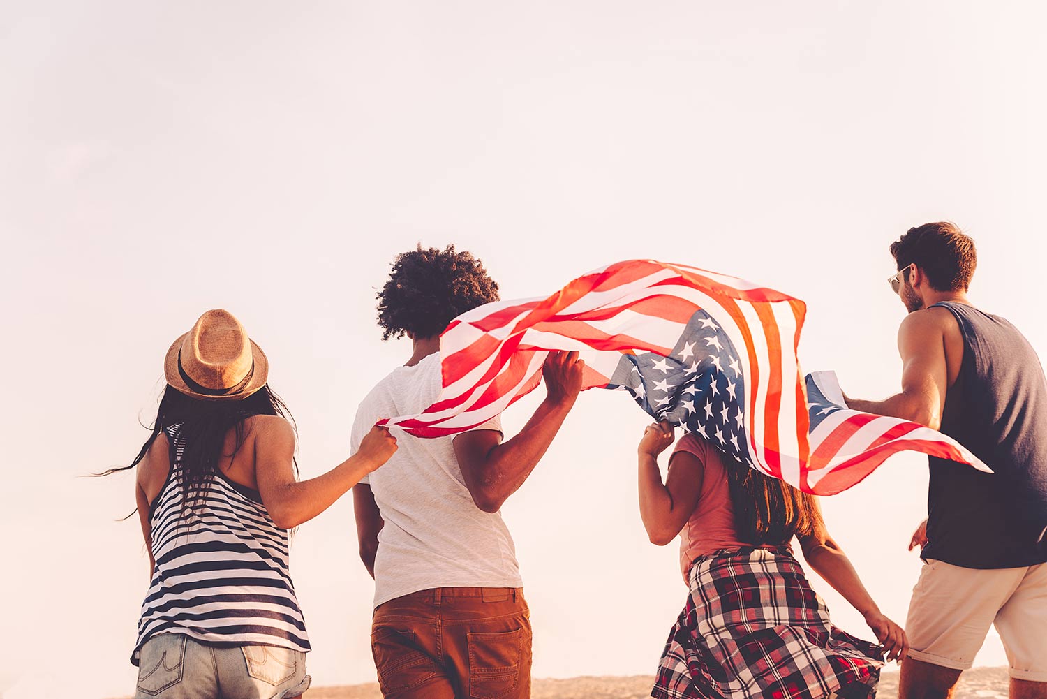 four friends on the beach holding an American Flag